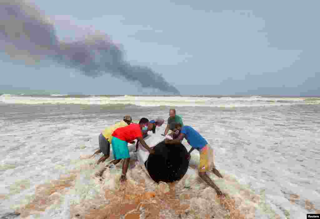 Smoke can be seen along the horizon from a fire onboard the MV X-Press Pearl container ship in the seas off the Colombo Harbor, while villagers push the cargo spilled from it onto a beach in Ja-Ela, Sri Lanka.