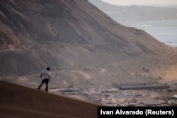 Seorang pria berlatih sandboarding di bukit pasir cagar alam 'Cerro Dragón' dengan latar belakang kota Iquique, di Gurun Atacama, Iquique, Chile, 29 Oktober 2024. (Foto: Ivan Alvarado/REUTERS)