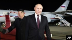Ruski predsednik Vladimir Putin korača dok se severnokorejski lider Kim Džong Un rukue sa članovima ruske deelegacije na međunrodnom aerodromu pored Pjongjanga, Severna Koreja, 19. juna 2024.