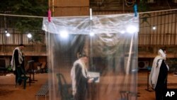 Ultra-Orthodox Jews keep social distancing and wear face masks during a morning prayer next to their houses as synagogues are limited to twenty people following the government's measures to help stop the spread of the coronavirus, in Bnei Brak, Israel.