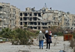 FILE - Residents of a suburban neighborhood on the edge of the northern Syrian city of Aleppo return to their homes to check the damage caused by fighting between regime forces and rebel fighters, Feb. 18, 2020.