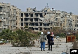 FILE - Residents of a suburban neighborhood on the edge of the northern Syrian city of Aleppo return to their homes to check the damage caused by fighting between regime forces and rebel fighters, Feb. 18, 2020.