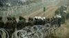 Polish soldiers and police watch migrants at the Poland/Belarus border near Kuznica, Poland, November 11, 2021, in this photograph released by the Territorial Defence Forces. 