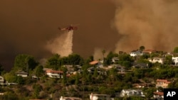 Un hélicoptère largue de l'eau sur les maisons alors que l'incendie de Palisades progresse dans le Mandeville Canyon, le samedi 11 janvier 2025, à Los Angeles.