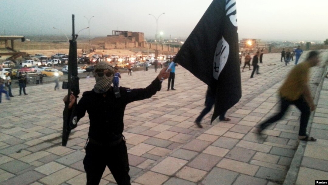 FILE - An Islamic State fighter holds the extremist group's signature flag and a weapon in the Iraqi city Mosul, June 23, 2014. Preparations are underway to wrest the city from IS control.