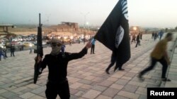 FILE - An Islamic State fighter holds up an IS flag and a weapon on a street in Mosul, Iraq, June 23, 2014.