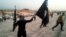 FILE - An Islamic State fighter holds up an IS flag and a weapon on a street in Mosul, Iraq, June 23, 2014.