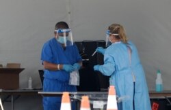 Healthcare workers put a vial containing a test swab into a bag after testing a driver at a drive-through coronavirus testing site outside of Hard Rock Stadium, June 26, 2020, in Miami Gardens, Fla.