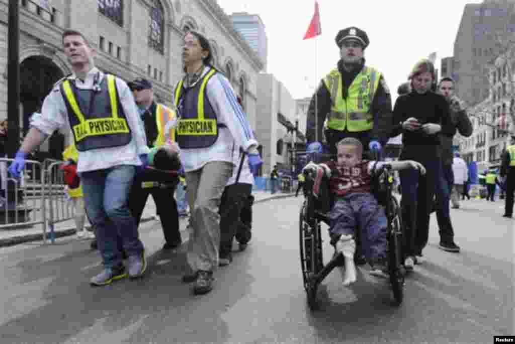 A Boston police officer wheels in injured boy down Boylston Street as medical workers carry an injured runner following an explosion during the 2013 Boston Marathon, April 15, 2013.