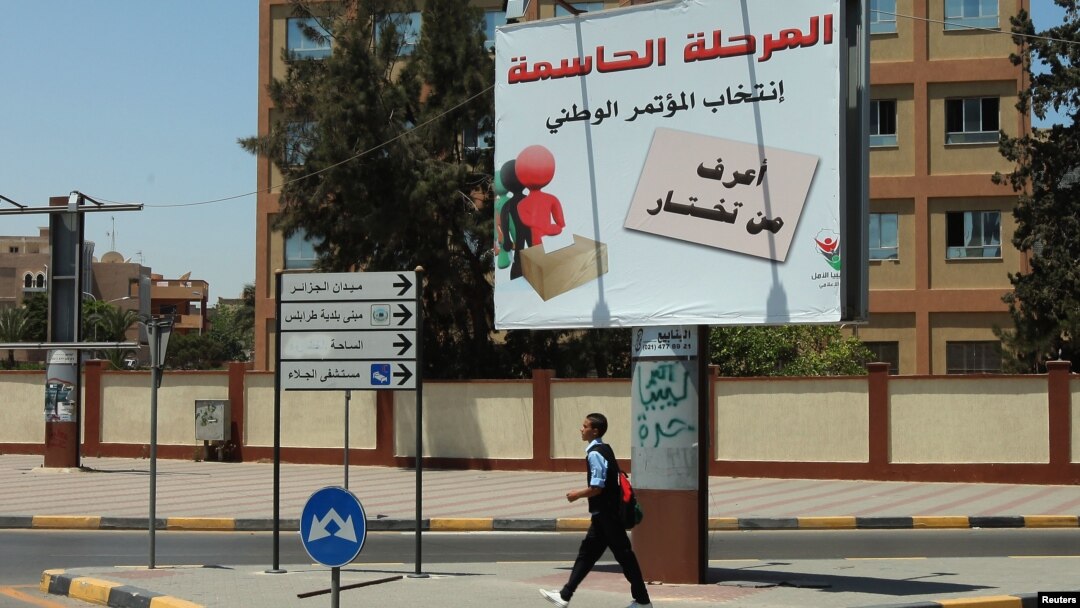 Seorang warga melintasi papan pengumuman Pemilu Libya yang bertuliskan "Tahapan Penting: Pemilu Parlemen Nasional - Anda Harus Tahu Siapa yang Anda Pilih" 19 Juni 2012. Komisi Pemilu Libya menunda Pemilu selama 18 hari dari tanggal ini. 