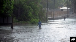 FILE: A man walks through a flooded road in the coast of the Indian Ocean Island of Mauritius Monday Feb. 20, 2023. Man-made climate change has been blamed for the surge in major storms in recent years.