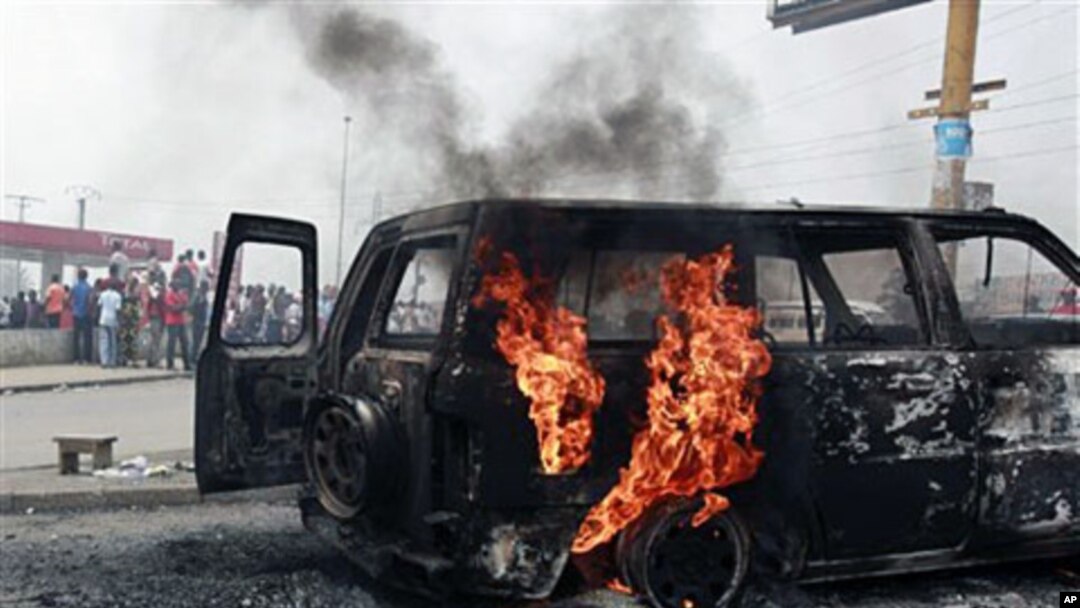 Local residents look on as a UN vehicle, set on fire by militant student supporters of Laurent Gbagbo, burns in the Riviera 2 neighborhood of Abidjan, 13 Jan 2011
