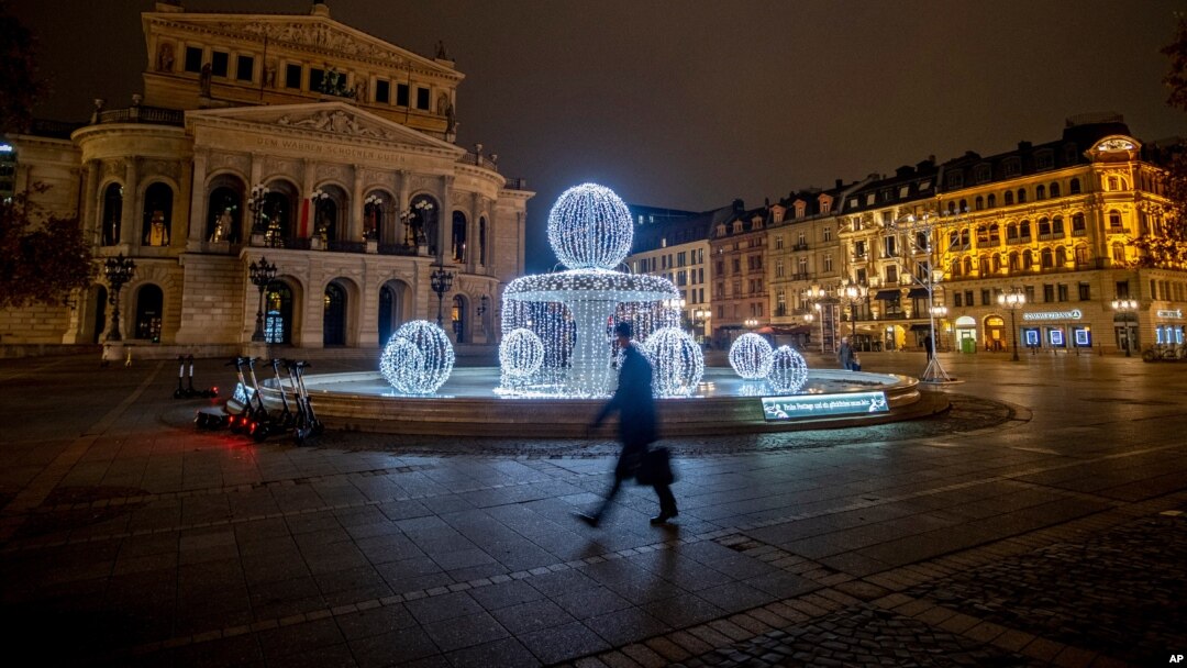 A man passes by the illuminated fountain in front of the Old Opera in Frankfurt, Germany, Dec. 10, 2020.