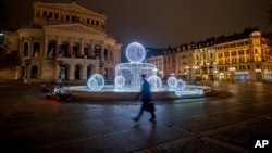 A man passes by the illuminated fountain in front of the Old Opera in Frankfurt, Germany, Dec. 10, 2020.