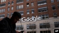 A man using a mobile phone walks past Google offices, Monday, Dec. 17, 2018, in New York. (AP Photo/Mark Lennihan)