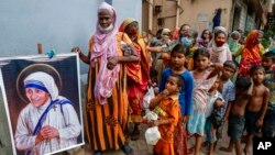 FILE - Homeless people gather beside a portrait of Saint Teresa, the founder of the Missionaries of Charity, to collect free food outside the order's headquarters in Kolkata, India, Aug. 26, 2021. 
