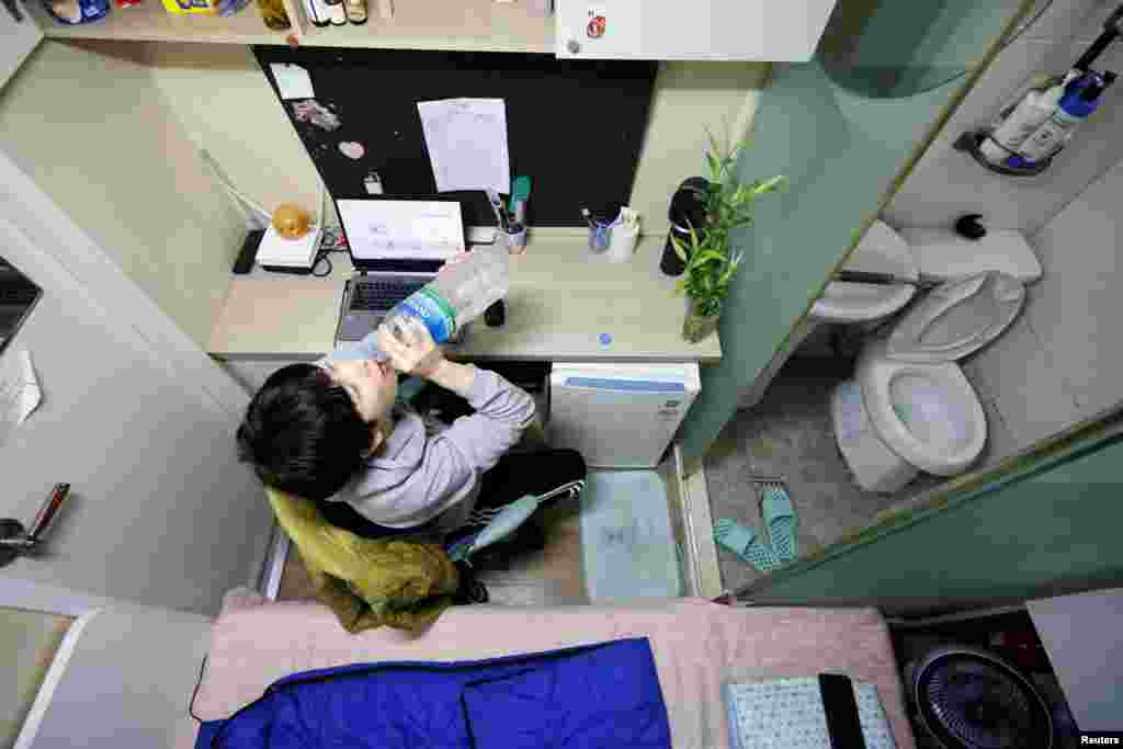 Kim Jae-hoon drinks water as he sits in his cubicle, called a goshi-won, where he lives in Suwon, South Korea.