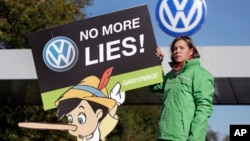 Aktivis Greenpeace memegang poster protes di depan gerbang pabrik Volkswagen di Wolfsburg, Jerman (25/9). (AP/Michael Sohn)