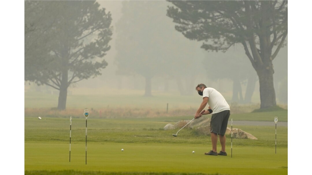 A golfer wears a face mask as he practices his putting at the smoke-shrouded Lake Tahoe Golf Course in South Lake Tahoe, Calif., Aug. 24, 2021.