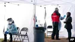 Un trabajador, a la izquierda, descansa por un segundo entre pacientes, mientras otra persona, a la derecha, se hace la prueba de COVID-19 en un sitio de test sin cita previa en Farragut Square, el jueves 23 de diciembre de 2021, a pocas cuadras de la Casa Blanca, en Washington.