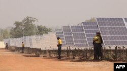 FILE - People stand next to solar panels of the solar energy power plant in Zagtouli, near Ouagadougou, Burkina Faso, Nov. 29, 2017, on its inauguration day.