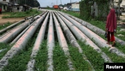 FILE - A girl walks on a gas pipeline running through Okrika community near Nigeria's oil hub city of Port Harcourt.