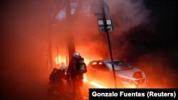 Des pompiers à côté d'une voiture entourée de flammes lors d'une manifestation contre un projet de loi controversé, à Paris, France, le 5 décembre 2020. 