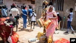 A woman receives foodstuffs including cooking oil, rice, sugar and soap, distributed by the government to families in need in the Guinaw Rails suburb of Dakar, Senegal, April 28, 2020. 