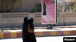 Veiled women walk past a billboard that carries a verse from Koran urging women to wear a hijab in the northern province of Raqqa, March 31, 2014. 