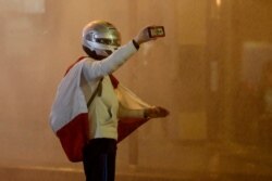 FILE - An anti-government protester is sprayed with a water cannon as he records video with his mobile phone during a protest in downtown Beirut, Lebanon, Jan. 22, 2020.