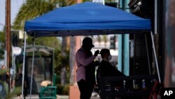 Un barbero corta el cabello a un cliente bajo una carpa al aire libre como una medida de seguridad para evitar el contagio del COVID-19 en Los Ángeles, California, 18 de agosto de 2020.