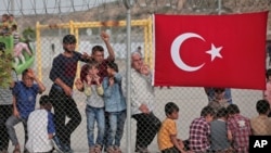 FILE - Migrants stand behind a fence at the Nizip refugee camp in Gaziantep province, southeastern Turkey, April 23, 2016. 