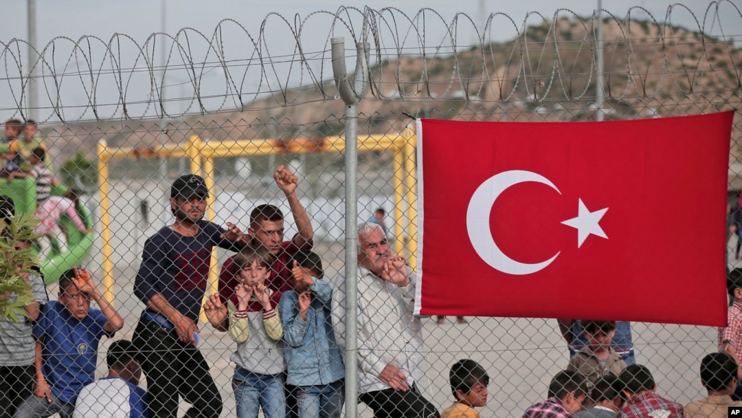 FILE - Migrants stand behind a fence at the Nizip refugee camp in Gaziantep province, southeastern Turkey, April 23, 2016. 