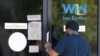 مردی در ایالت میسیسپی فرم تقاضای بیمه بیکاری را از نگهبان از پشت در شیشه ای مرکز کاریابی دریافت می کند. آرشیو،، ۲ آوریل ۲۰۲۰