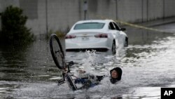 Un ciclista cae mientras intentaba atravesar las aguas inundadas cerca de un automóvil varado, el viernes 1 de septiembre de 2023, en Las Vegas.