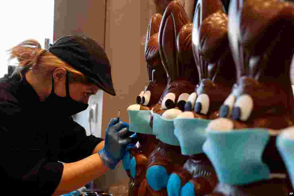 A sweet shop employee wearing a protective mask prepares chocolate Easter bunnies with face masks in Lykovrisi, northern Athens, Greece.