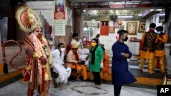 Seorang pria berpakaian seperti dewa monyet Hindu, Hanuman, berdiri di sebuah kuil pada hari pertama dibukanya kembali kuil itu setelah ditutup akibat pandemi corona di New Delhi, India, Senin, 8 Juni 2020.