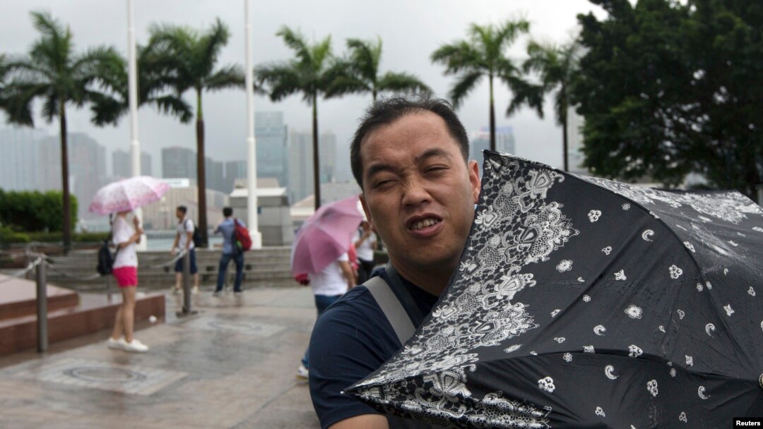 Seorang pria berusaha menahan terpaan angin dengan payungnya di Lapangan Golden Bauhinia, saat topan Utor mendekati Hong Kong (14/8).