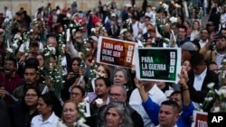 La gente sostiene flores y carteles durante un evento para recordar a los exguerrilleros y líderes sociales que han sido asesinados desde la firma de un acuerdo de paz en 2016 entre los rebeldes de las FARC y el gobierno, en Bogotá, Colombia, el martes 20 de febrero de 2024.