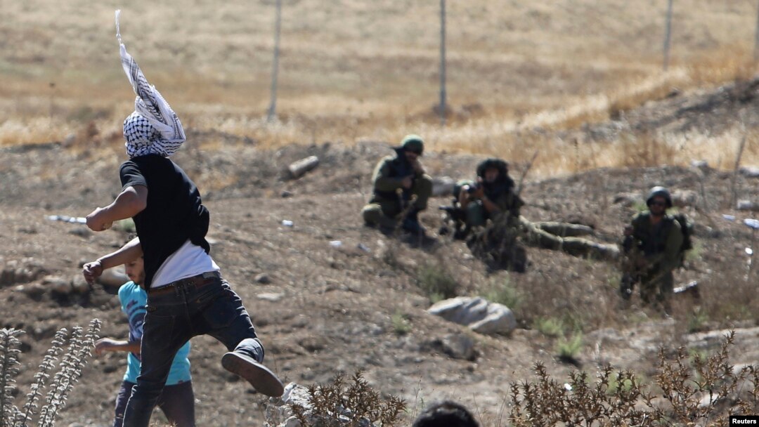 Demonstran Palestina melempar batu ke arah tentara Israel dan polisi perbatasan dalam protes mengecam ofensif Israel di Gaza, di kota Hawara, Tepi Barat (25/7/2014). 
