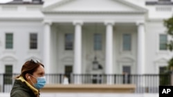 FILE - A woman wearing a face mask walks past the White House in Washington, April 1, 2020.