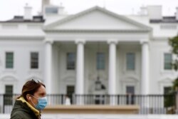 FILE - A woman wearing a face mask walks past the White House in Washington, D.C., April 1, 2020.