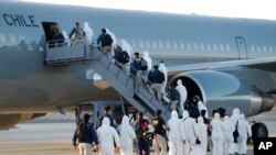 Migrantes venezolanos y colombianos que son deportados usan equipo de protección mientras caminan en línea con la policía para abordar un avión en el Aeropuerto Internacional General Diego Aracena Aguilar en Iquique, el 10 de febrero de 2021.