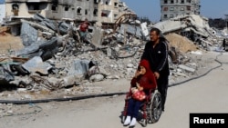 A Palestinian man pushes a child on a wheelchair amidst the rubble of buildings destroyed during the Israeli offensive, amid a ceasefire between Israel and Hamas, in Rafah