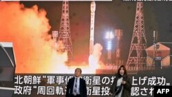 Pejalan kaki berjalan melewati layar yang menampilkan peluncuran satelit pengintai Korea Utara 'Malligyong-1', di distrik Akihabara Tokyo pada 22 November 2023. (Foto: AFP)