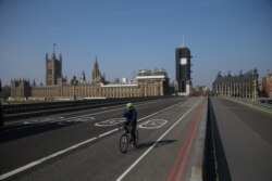 FILE - A cyclist crosses a near-empty Westminster Bridge with the Houses of Parliament in the background, amid the coronavirus outbreak, in central London, Britain, April 9, 2020.