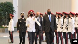 FILE - In this photo provided by the Singapore Ministry of Defense, U.S. Defense Secretary Lloyd J. Austin along with Singapore Defense Minister Ng Eng Hen, back, review an honor guard at the Ministry of Defense, July 27, 2021.