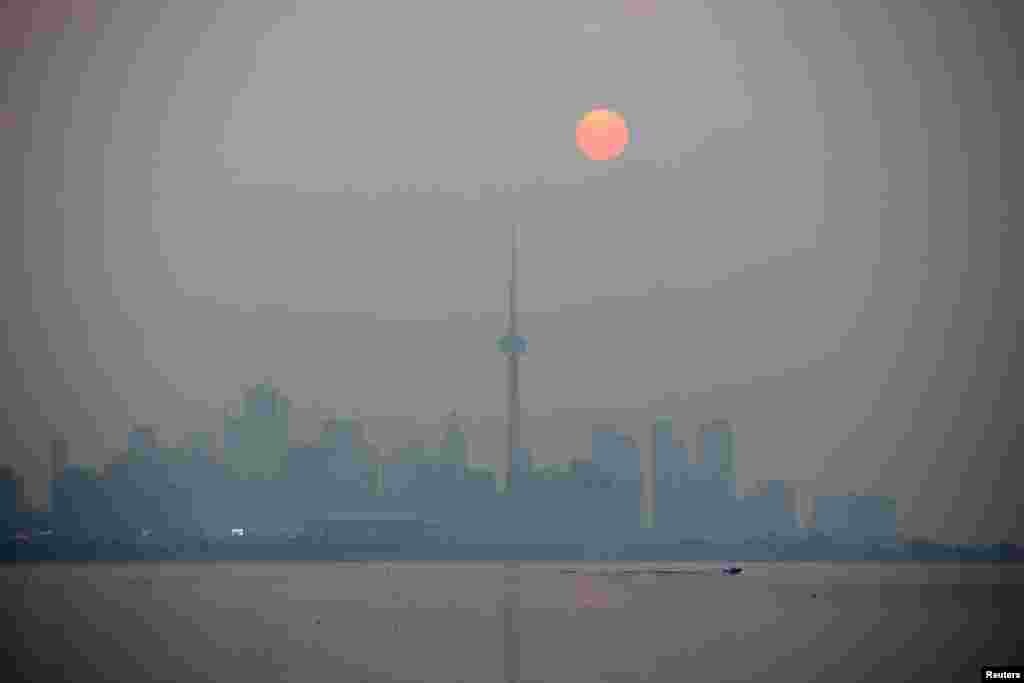 The sun rises through a cover of wildfire smoke above the CN Tower and downtown skyline in Toronto, Ontario, Canada.