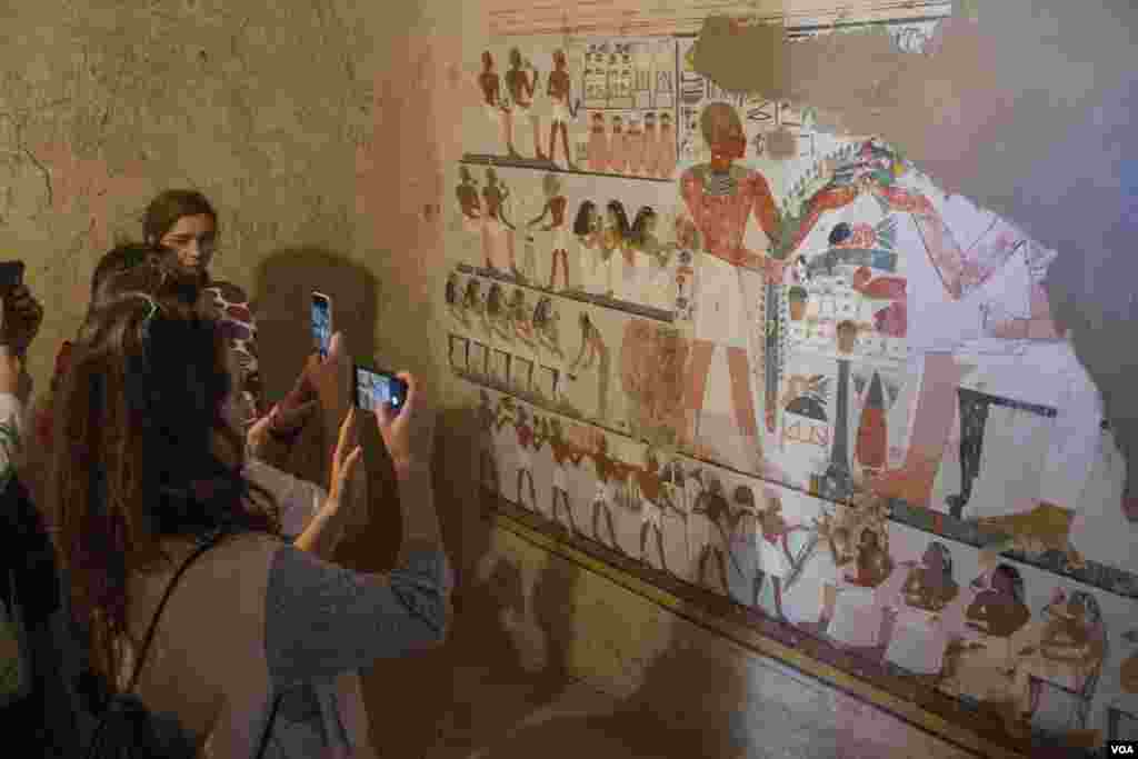 Para wisatawan mengambil foto mural yang menggambarkan prosesi pemakaman di makam yang baru ditemukan di Kampp 161, di pekuburan Draa Abul Naga, di Tepi Barat Luxor, Mesir, 9 Desember 2017. (H. Elrasam/VOA)