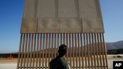 FILE - A U.S. Border Patrol agent looks at one of border wall prototypes in San Diego, June 28, 2018. 